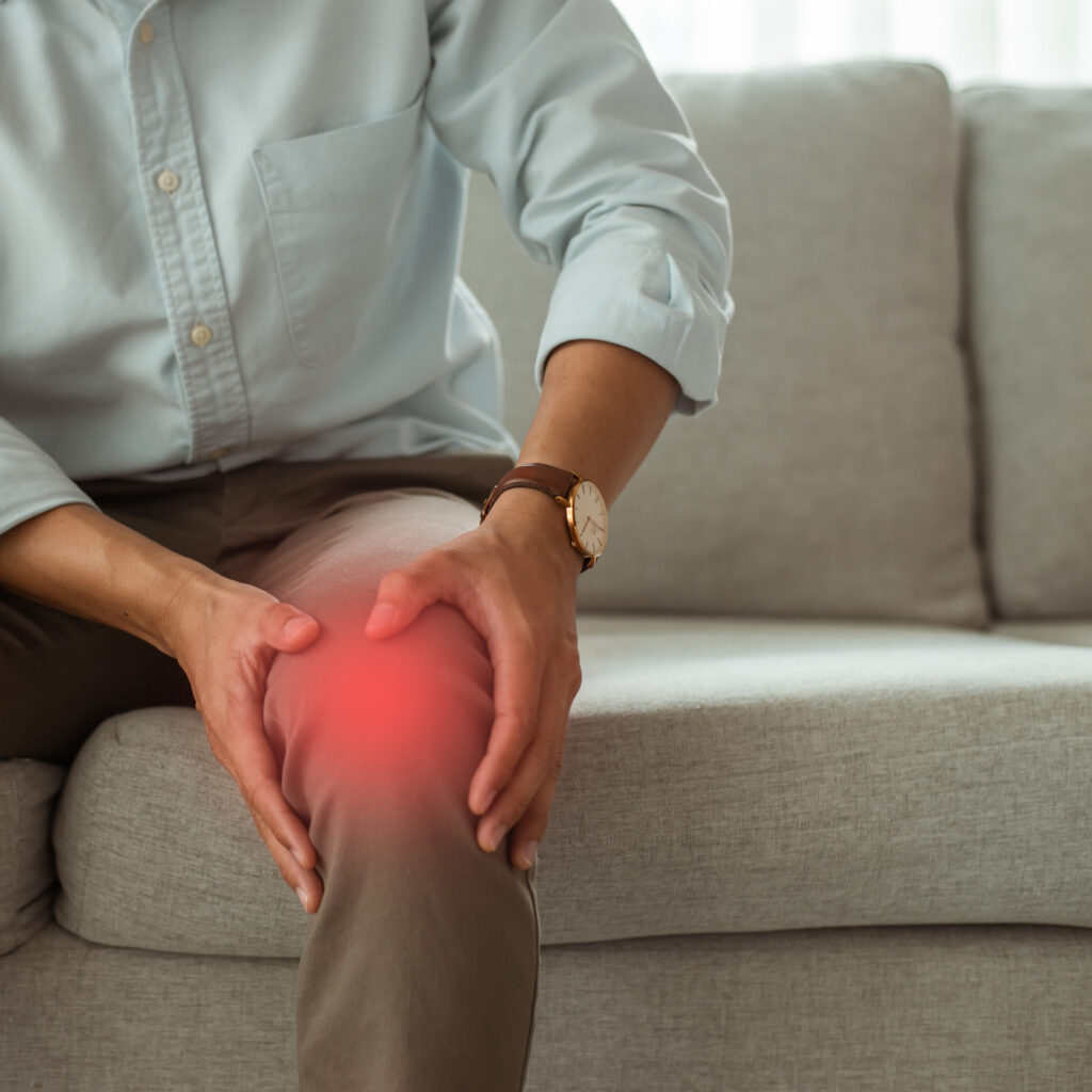 young man sat sofa living room home was holding his knees with both hands he was suffering from knee pain was unhappy daily life he had be healed quickly